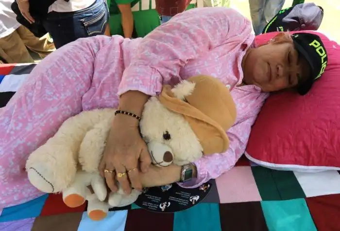 Una mujer en pijama, con gorra de policía y sosteniendo un osito de peluche, finge estar dormida durante la celebración del Día Mundial de la Pereza en Itagüí, Colombia, el 18 de agosto de 2024. (Foto de JAIME SALDARRIAGA / AFP)