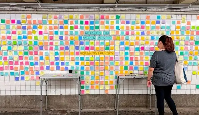 Una usuario del metro se detiene a escribir y leer los pensamientos de las personas plasmados en el muro del metro de Nueva York. / AFP